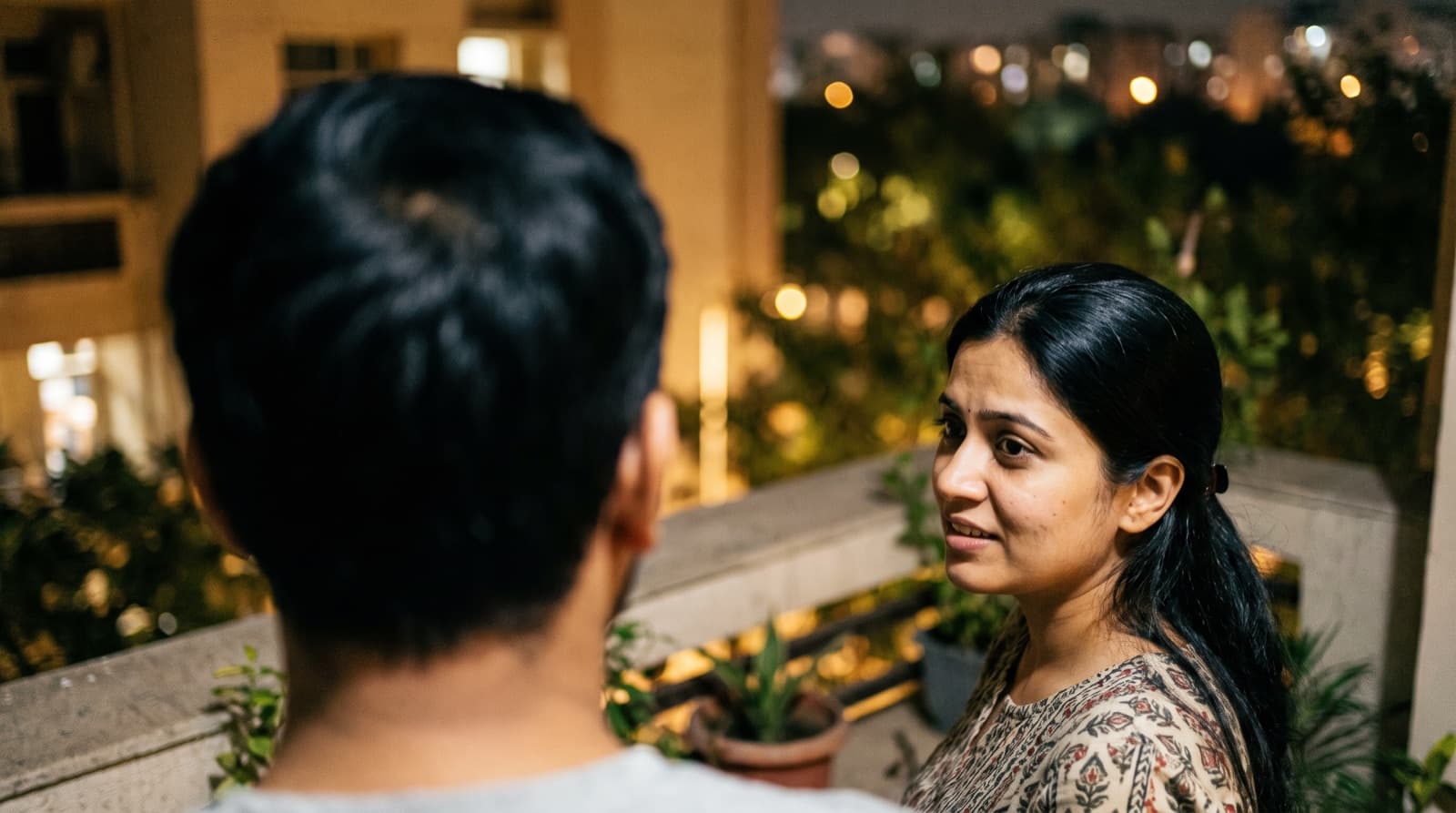 A couple sitting close on a balcony, looking uncertain